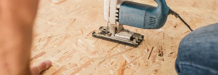 Person sägt Holzplatte mit Stichsäge